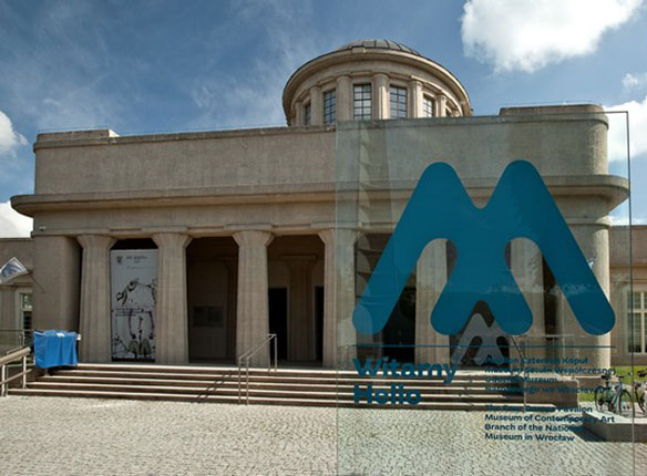 wejście do Pawilonu Czterech Kopuł, przed schodami logo Muzeum (niebieska litera M) z napisami Witamy Hello