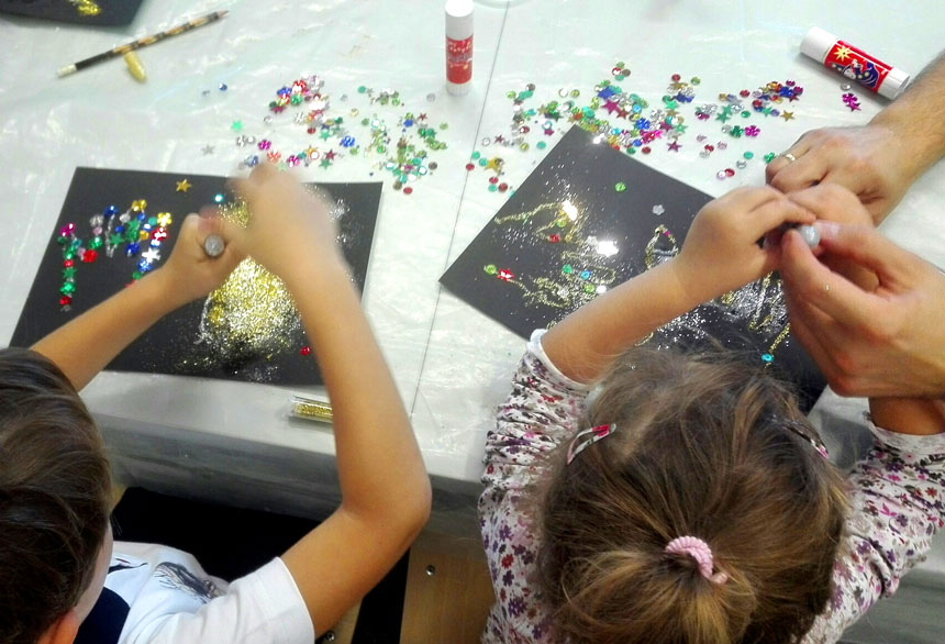 Dzieci posypują brokatem odrysowany ślad dłoni na kartce