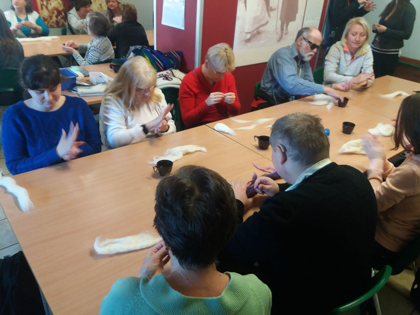 foto: uczestnicy zajęć siedzą wokół dużego stolu i z wełny rolują wałki, z których będzie tworzony filc – inne ujęcie
