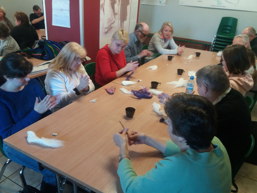 foto: uczestnicy zajęć siedzą wokół dużego stolu i z wełny rolują wałki, z których będzie tworzony filc