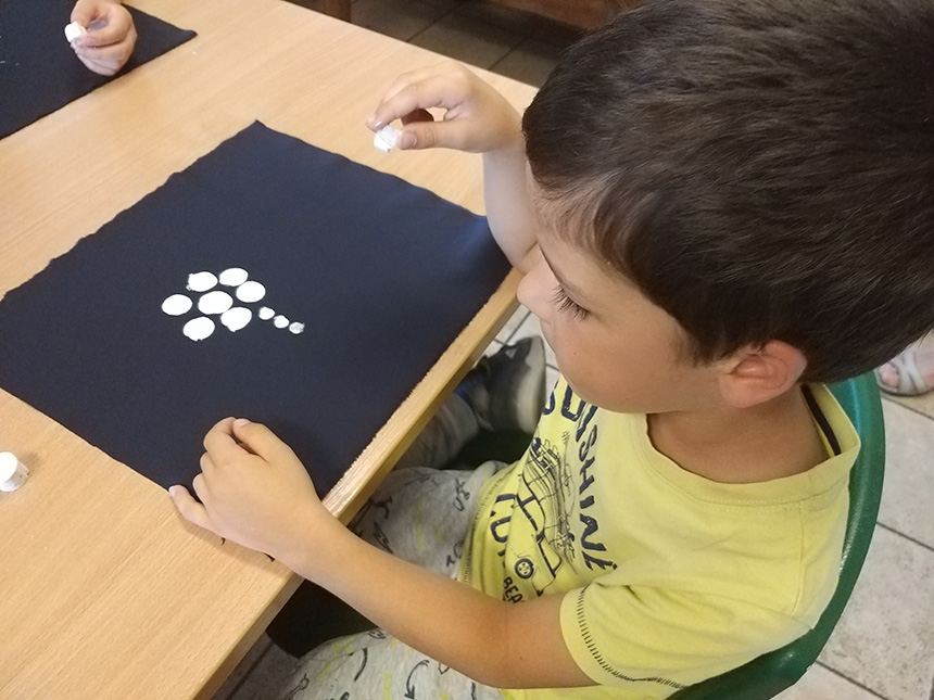 chłopiec stempluje czarny materiał białą kredą, jako praca powstaje kwiatek