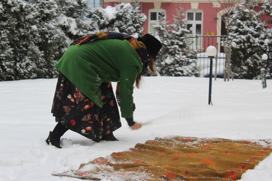 Pochylona nad dywanem rozłożonym na śniegu kobieta trzepie go energicznie