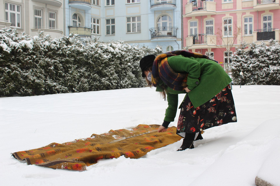Ciepło ubrana kobieta stoi z trzepaczką nad dywanem położonym na świeżym śniegu