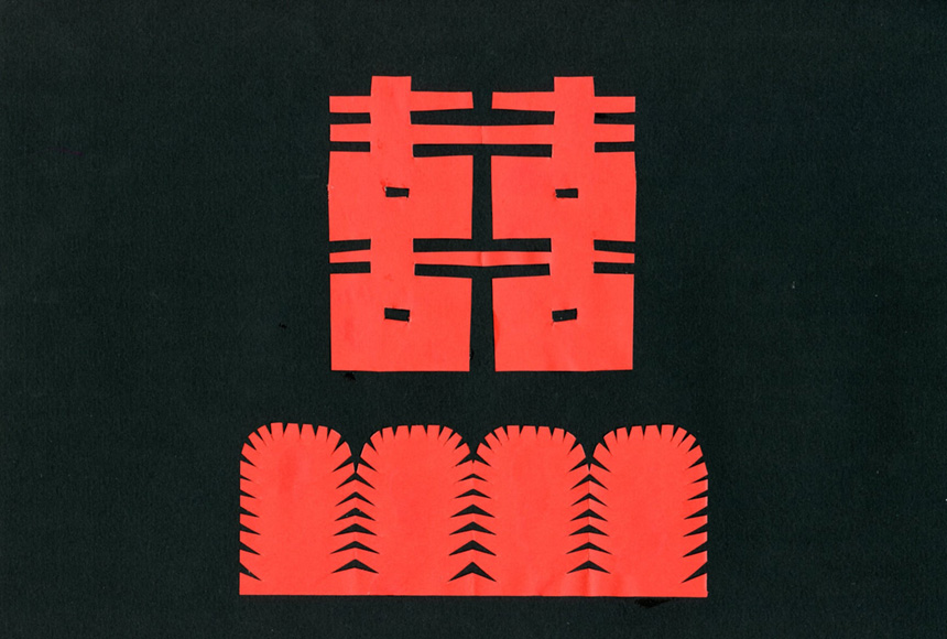 Chiński symbol xi (podwójny) oznaczający szczęście wycięty z czerwonego papieru na czarnym tle. Pod symbolem symetrycznie wycięte krzaczki z czerwonego papieru.