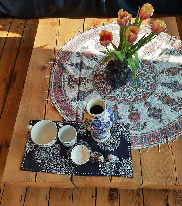 Zadrukowana w niebieskie wzory serwetka leży na stole w towarzystwie biało-niebieskiej zastawy stołowej i wazonu z tulipanami