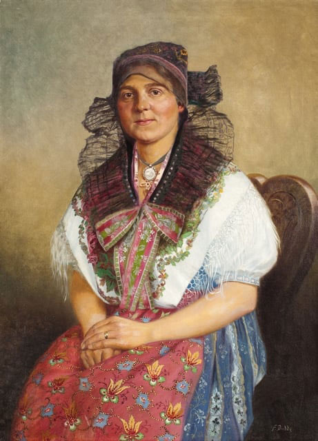 Kobieta siedząca na krześle w stroju regionalnym. Jasnozielone tło. Na głowie czepiec z koronką okalającą twarz, biała koszula z krótkim rękawem i chusta okrywająca gors. Niebiesko-biała spódnica okryta czerwonym fartuchem z kolorowymi kwiatami