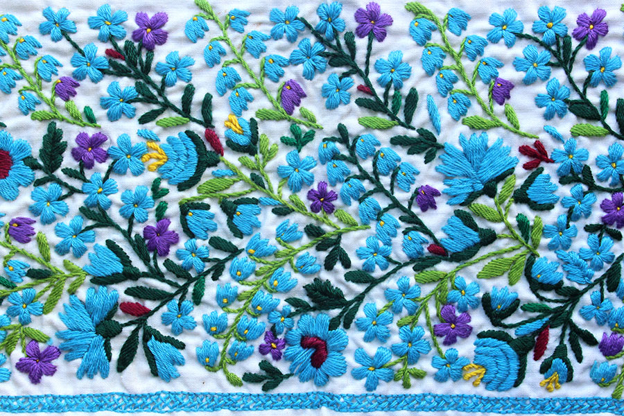 Na białej tkaninie wyhaftowane niezapominajki i niebieskie dzwonki. Kwiatki zostały rozmieszczone bardzo gęsto – zbliżenie na detal