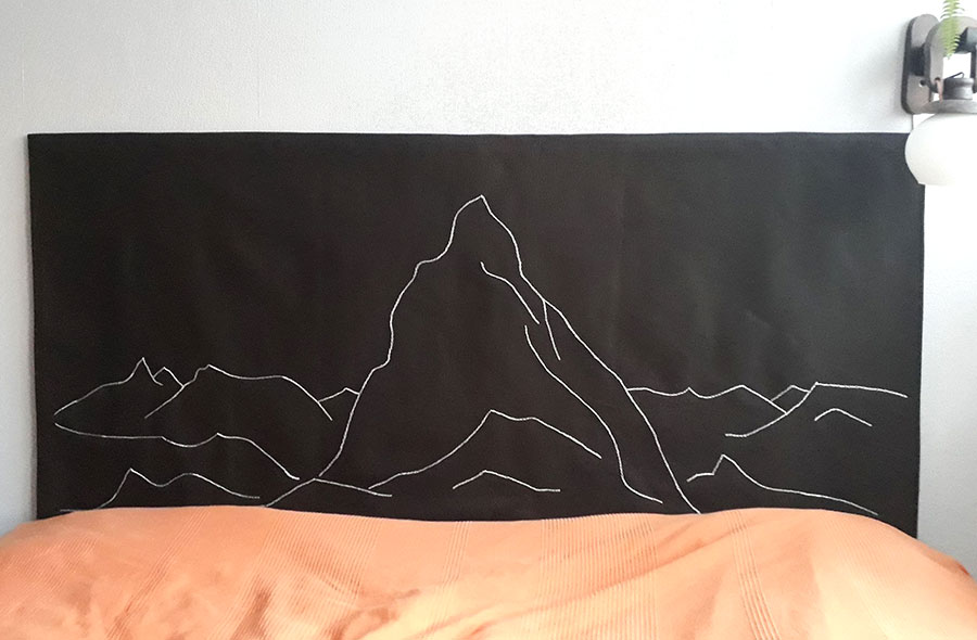 Na czarnej tkaninie nad łóżkiem wyszyte są białym ściegiem zarysy gór