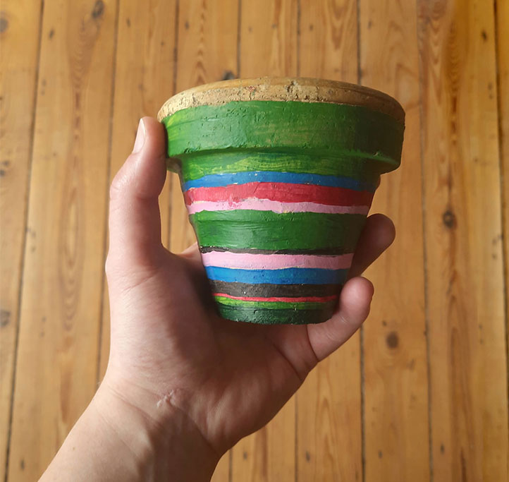 ceramiczna doniczka pomalowana w paski zielono-czerwono-różowo-błękitno-brązowe