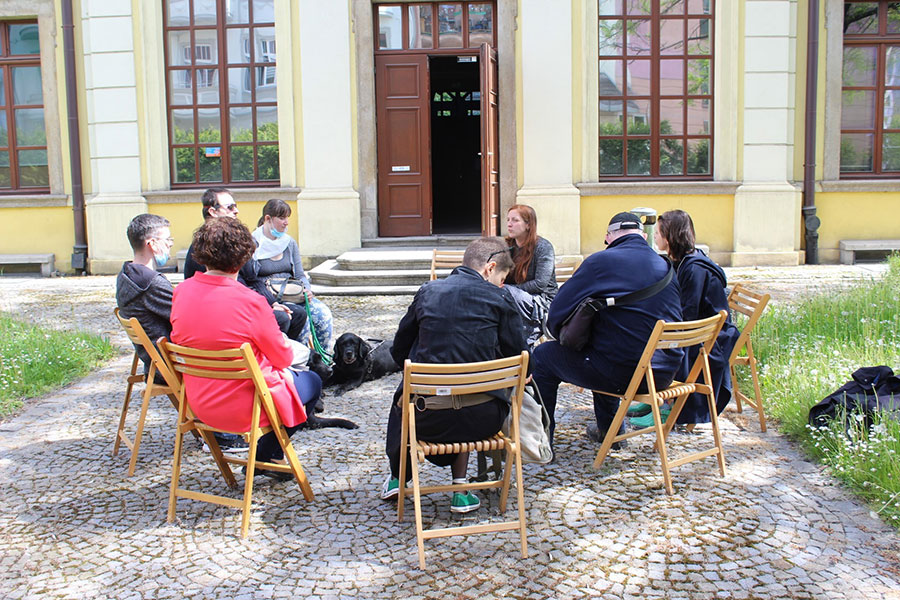 Spotkanie przy Muzeum Etnograficznym – zebrani siedzą na krzesłach w muzealnym ogrodzie