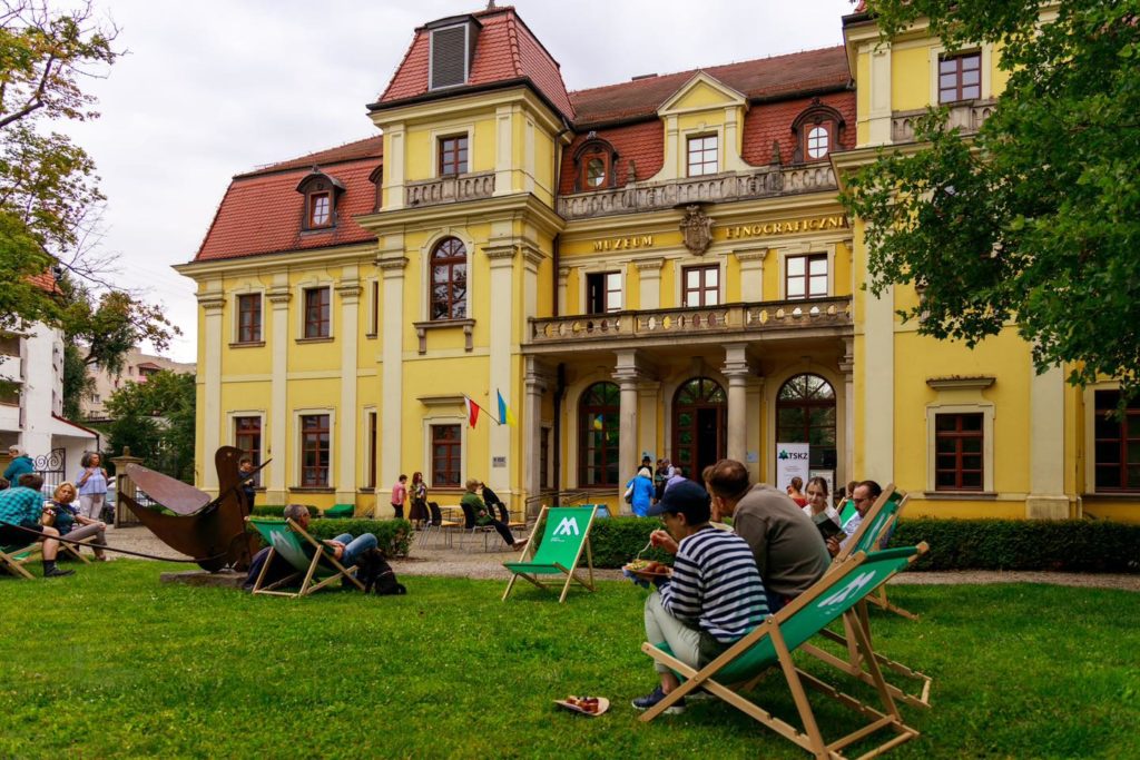 Budynek Muzeum Etnograficznego we Wrocławiu. Przed nim osoby na leżakach w trakcie posiłku.